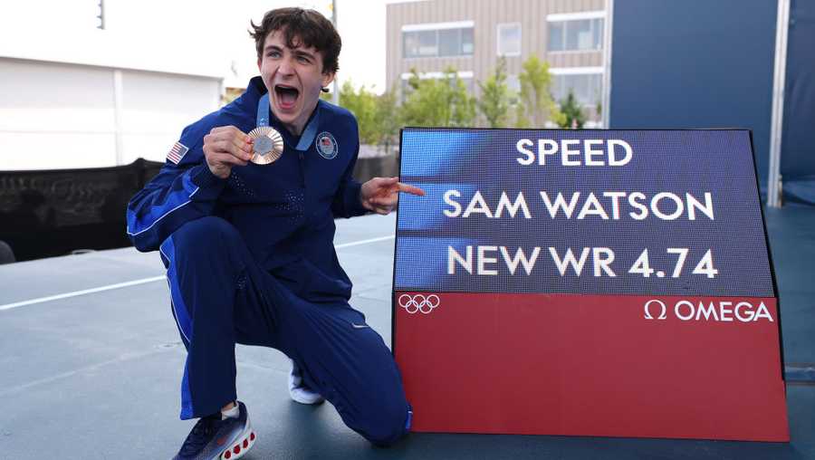 Bronze medalist Sam Watson of Team United States poses alongside a screen with his world record time of "4.74" during the Sport Climbing medal ceremony